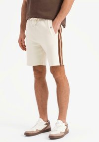 Vita shorts med bruna sidofält, elastisk midja och fickor. Bärs med vita och bruna sneakers. Slät tyg, avslappnad passform.