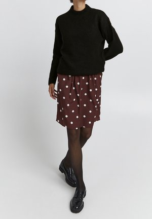 Pull en maille noir avec un col rond, associé à une jupe bordeaux à pois et des mocassins noirs, présenté sur un fond neutre.