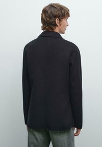 Black wool-blend coat with a structured design, wide lapels, and straight-cut silhouette. Features a smooth texture and minimal detailing.