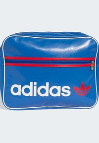 Modra sintetična torba z izrazitim belim logotipom »adidas«, rdečimi poudarki in žepom z zadrgo. Ima sijočo teksturo in detajlce iz trakov.