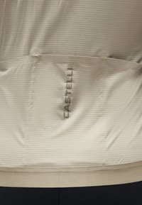 Tissu texturé beige clair avec un logo vertical gris foncé « CASTELLI » centré entre deux coutures horizontales.