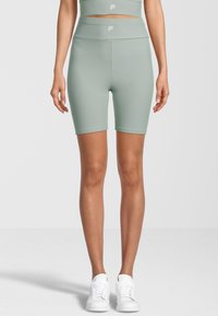 Shorts a coste verde menta con vita alta. Presentano una texture liscia e un logo bianco sulla cintura. Abbinati a sneakers bianche.