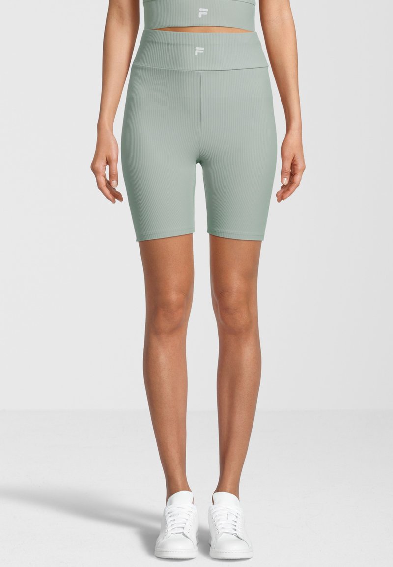 Shorts a coste verde menta con vita alta. Presentano una texture liscia e un logo bianco sulla cintura. Abbinati a sneakers bianche.