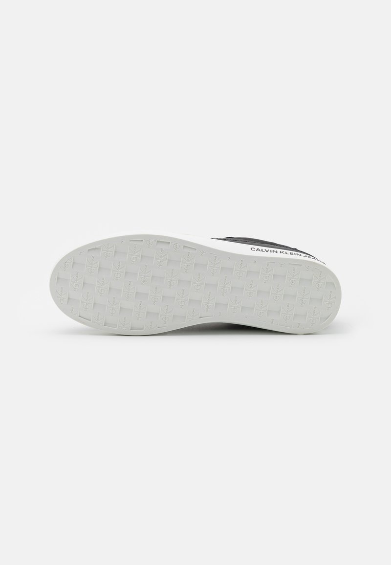 Sneaker noir avec une semelle en caoutchouc texturé. Présente une semelle blanche avec un motif de bande de roulement et un logo sur le côté.