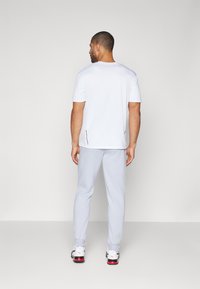 Men's white short-sleeve t-shirt with a round neck, paired with light gray pants and black and white sneakers, showcasing a relaxed fit.