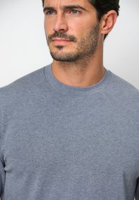 Maglione grigio a collo rotondo realizzato in tessuto morbido. Presenta un colletto a costine, una superficie liscia e una vestibilità classica adatta per un abbigliamento casual.
