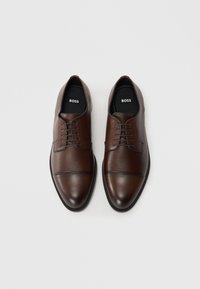 Pair of polished brown leather dress shoes with lace-up front and cap-toe design, branded "BOSS" on black insoles, set on white background.