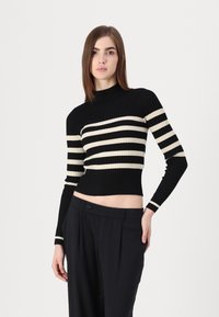 Μαύρο και κρεμ ριγέ ρεβιέ φανελάκι με ψεύτικο λαιμό και εφαρμοστή σχεδίαση, σε συνδυασμό με ψηλόμεσες μαύρες παντελόνες. Υφή από πλεκτό ύφασμα.