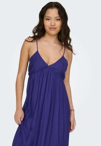 Vestido maxi morado sin mangas con escote en V, tejido fluido, cintura fruncida y tirantes finos. Textura suave con un ligero brillo.