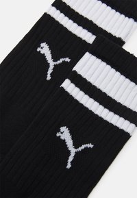 Czarne skarpetki sportowe z prążkowaną strukturą, białymi paskami na górze i białym logo Pumy z boku.