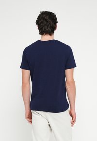 Tmavomodré bavlnené tričko s krátkymi rukávmi a okrúhlym výstrihom, s hladkou textúrou a voľným strihom. Pohľad zozadu ukazuje jednoduchý dizajn.