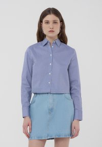 Camicia a maniche lunghe con bottoni, ritagliata, a righe verticali blu e bianche, con colletto, abbinata a una gonna di jeans blu chiaro.