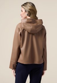 Jachetă din piele ecologică maro, cu glugă, având o textură netedă și un design ușor scurtat. Detalii cu cusături vizibile pe spate.