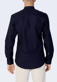Camicia a maniche lunghe blu navy con colletto button-down, schiena dritta e maniche con polsini. Tessuto liscio con una silhouette aderente.