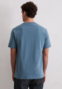 T-shirt z krótkim rękawem i okrągłym dekoltem w stonowanym niebieskim kolorze, wykonany z miękkiej bawełny. Gładka faktura bez widocznych wzorów czy akcentów.