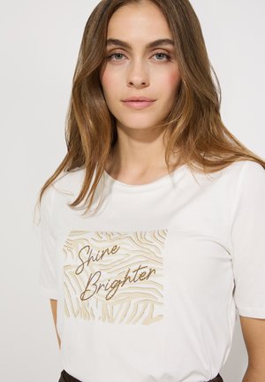White t-shirt featuring a textured gold graphic with the text "Shine Brighter" in a wavy pattern. Short sleeves and a relaxed fit.