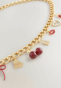 Kuldne kett, millel on mitmed ripatsid: punased kirsiid, süda, huulepulk, huuled ja pärligrupid. Sile ja läikiv tekstuur.