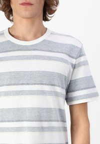 T-shirt rayé en gris et blanc avec des accents jaunes, doté d'un col rond et de manches courtes. Tissu texturé avec un tissage semblable à un maillage.