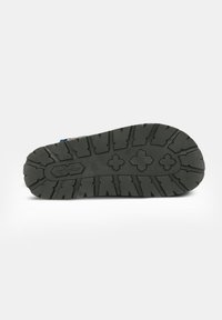 Suola di scarpa in gomma nera con scanalature profonde, incluse forme geometriche e logo inciso. Finitura liscia sul bordo superiore.