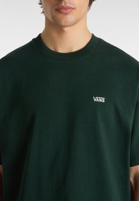 Tmavě zelené tričko s krátkým rukávem vyrobené z bavlny, s malým bílým vyšívaným logem "VANS" na hrudi. Měkká textura, kulatý výstřih.