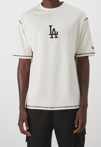 Krémové tričko s krátkým rukávem vyrobené z bavlny, s námořnickým vyšitým logem "LA" na hrudi a kontrastním černým prošíváním na rukávech a lemu.