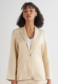 Beige linnen blazer met een enkele knoopsluiting, notch revers, twee voorzakken en lange mouwen, met een gladde textuur.