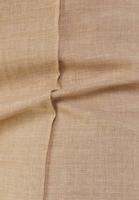 Beige Stoff mit einer subtilen Textur, der eine glatte Oberfläche aufweist und eine Naht zeigt, die die weiche, gewebte Struktur betont.