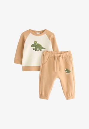 Completo beige per bambino in due pezzi con grafica di dinosauro su maglia bianca e beige a maniche lunghe e pantaloni coordinati con vita elasticizzata e tasche.
