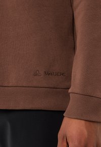 Felpa Vaude marrone con polsini e orlo a costine, caratterizzata da una texture sottile. Dettagli del logo ricamati sul davanti.