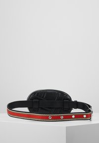 Sac banane en cuir noir avec un matelassage détaillé et une sangle en tissu ajustable ornée de rayures rouges, beiges et noires, avec une boucle en métal.