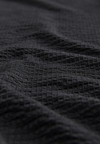 Un tissu noir texturé présentant un motif en grille, présenté en position drapée. Le matériau semble doux avec une surface légèrement inégale.