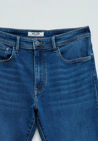Tamno plave traperice s dizajnom pet džepova, s kopčanjem na dugme i kontrastnim narančastim šavovima. Oznaka glasi "Salsa Jeans."