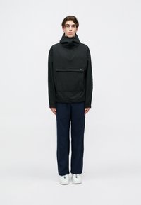 Μαύρος, κουκούλα πλεκτή μπλούζα με φερμουάρ στον λαιμό και μπροστινή τσέπη; διαθέτει υφασμάτινη υφή και συνδυάζεται με ναυτικές παντελόνες και λευκά αθλητικά παπούτσια.