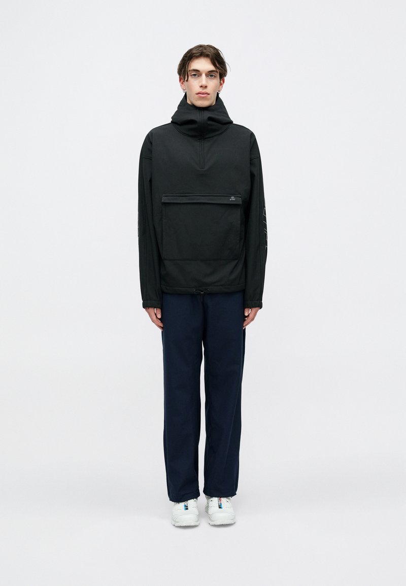 Μαύρος, κουκούλα πλεκτή μπλούζα με φερμουάρ στον λαιμό και μπροστινή τσέπη; διαθέτει υφασμάτινη υφή και συνδυάζεται με ναυτικές παντελόνες και λευκά αθλητικά παπούτσια.