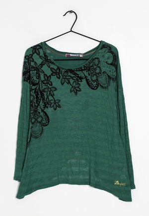 Maglia verde a maniche lunghe in tessuto testurizzato, con ricami floreali neri lungo il colletto. L'orlo è leggermente curvo.