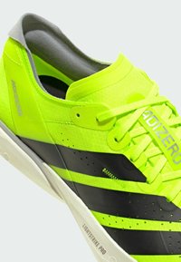 Neon keltainen urheilukenkä mustilla raidoilla, teksturoidulla päällisellä ja litteillä nauhoilla. Varustettu pehmustetulla kauluksella ja "LIGHTSTRIKE PRO" -brändäyksellä pohjassa.