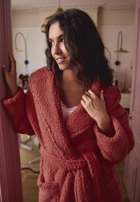 Cozy, textured, long-sleeve robe in soft, deep rose color with a belted waist and patch pockets. Features a plush, fuzzy fabric.