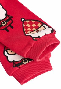 Červené textilní dlouhé rukávy s motivy kresleného Santa Clause a kloboukem s diamantovým vzorem. Žebrované manžety zajišťují těsný střih.