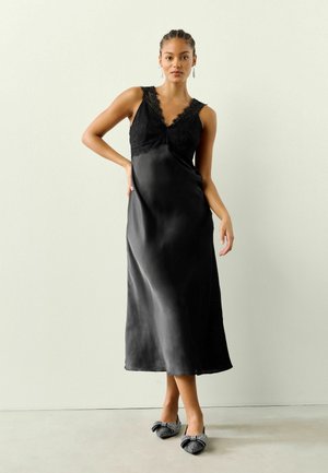 Black satin dress with lace trim at the neckline, featuring a V-shaped bodice and long flowy skirt; paired with embellished black shoes.