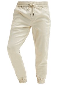 Pantalon de jogging beige en coton avec taille élastique, cordon de serrage, poches latérales et poignets élastiques.