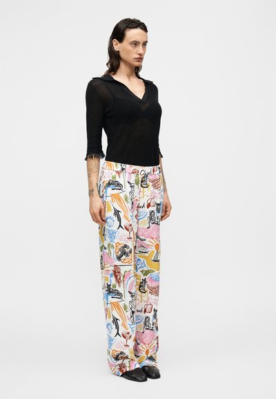 Μαύρο πλεκτό τοπ με V-λαιμόκοψη και μανίκια 3/4, συνδυασμένο με φαρδι ά, εμπριμέ παντελόνια που φέρουν πολύχρωμες ζωγραφιές σε ανοιχτό φόντο.