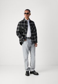 Svart og hvit rutet skjorte med to frontlommer, hvit t-skjorte, lyseblå jeans og svarte klumpete støvler, accessorert med solbriller.
