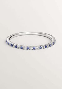 Anillo de plata con una fila de piedras preciosas azules y transparentes alternadas, montadas en una banda lisa, pulida para un acabado brillante.