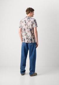 Short-sleeve shirt with a light beige base, featuring a colorful horse print, paired with loose-fitting blue denim jeans and sandals.