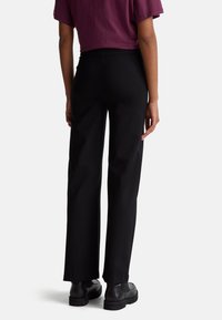 Černé kalhoty s širokými nohavicemi z hladké látky, s vysokým pasem a zadními kapsami, spárované s černými botami a vínovým topem.