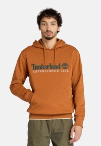 Felpa marrone con tasca a marsupio, caratterizzata da una grafica verde e bianca "Timberland Established 1973" sulla parte anteriore. Tessuto in misto cotone.