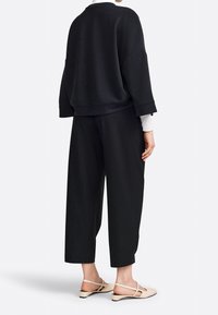 Svart överdimensionerad sweatshirt med sänkta axlar, kombinerad med lösa svarta byxor och beige slingbacks. Mjukt tyg med avslappnad passform.