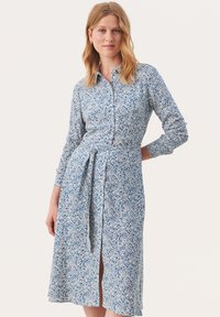 Abito bottonato blu a fiori con maniche lunghe, cintura in vita, bordo sopra il ginocchio e una leggera fessura; realizzato in un tessuto leggero.