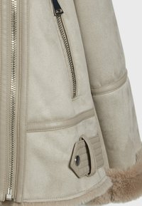 Beige Kunstwildlederjacke mit Reißverschluss, Seitentasche und strukturiertem Kunstfellbesatz am Saum. Verfügt über dekorative Nähte und Knöpfe.