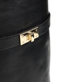 Czarna skórzana torba z metalowym zapięciem w kolorze złotym, gładką teksturą i wąskim paskiem wokół górnej części.